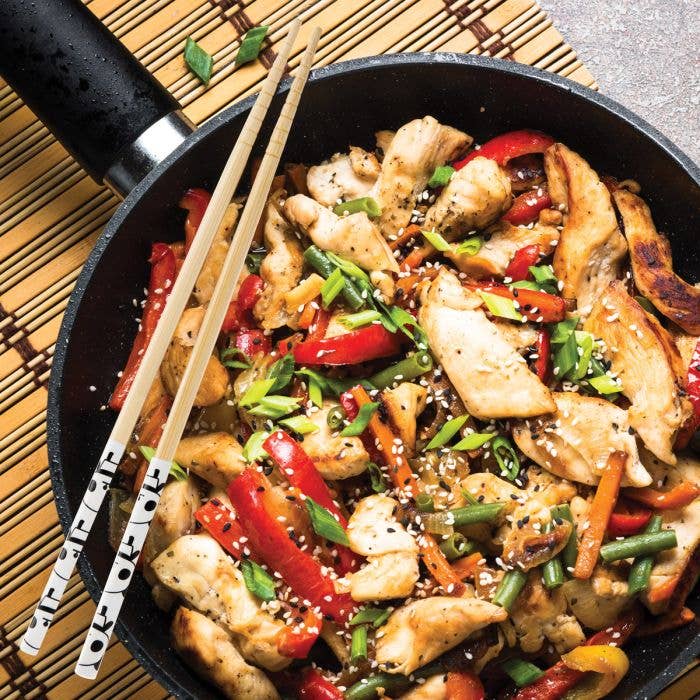 Fried chicken with vegetables in a pan with chopsticks on a wooden mat