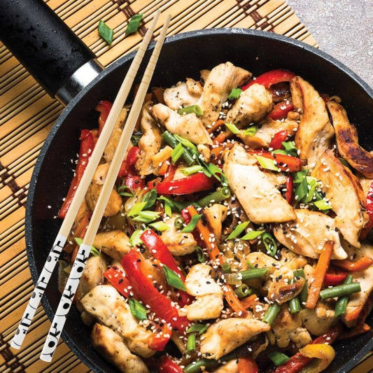Fried chicken with vegetables in a pan with chopsticks on a wooden mat