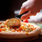 Classic Pizza Cutter being kused to ut a pizza on a brown table. 