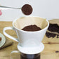 Coffee brewing process with a white pour-over coffee maker on a wooden surface.