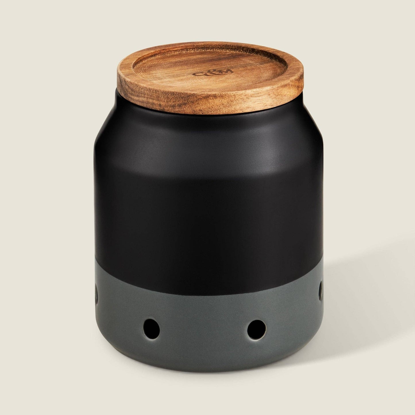 Black ceramic garlic keeper with a wooden lid on a beige background