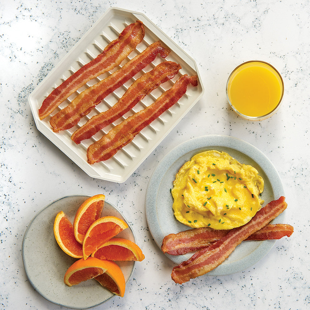 Breakfast setting with bacon, eggs, orange slices, and juice on a speckled countertop.