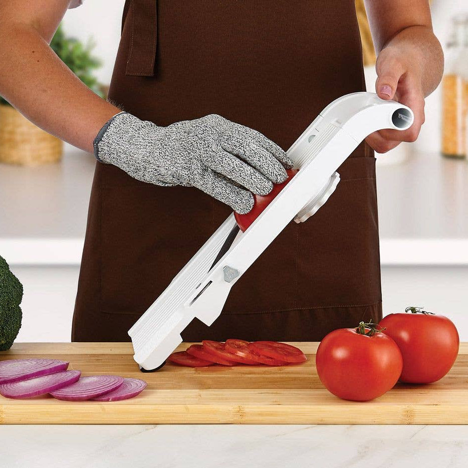 Person using a slicer on a kitchen counter with vegetables.