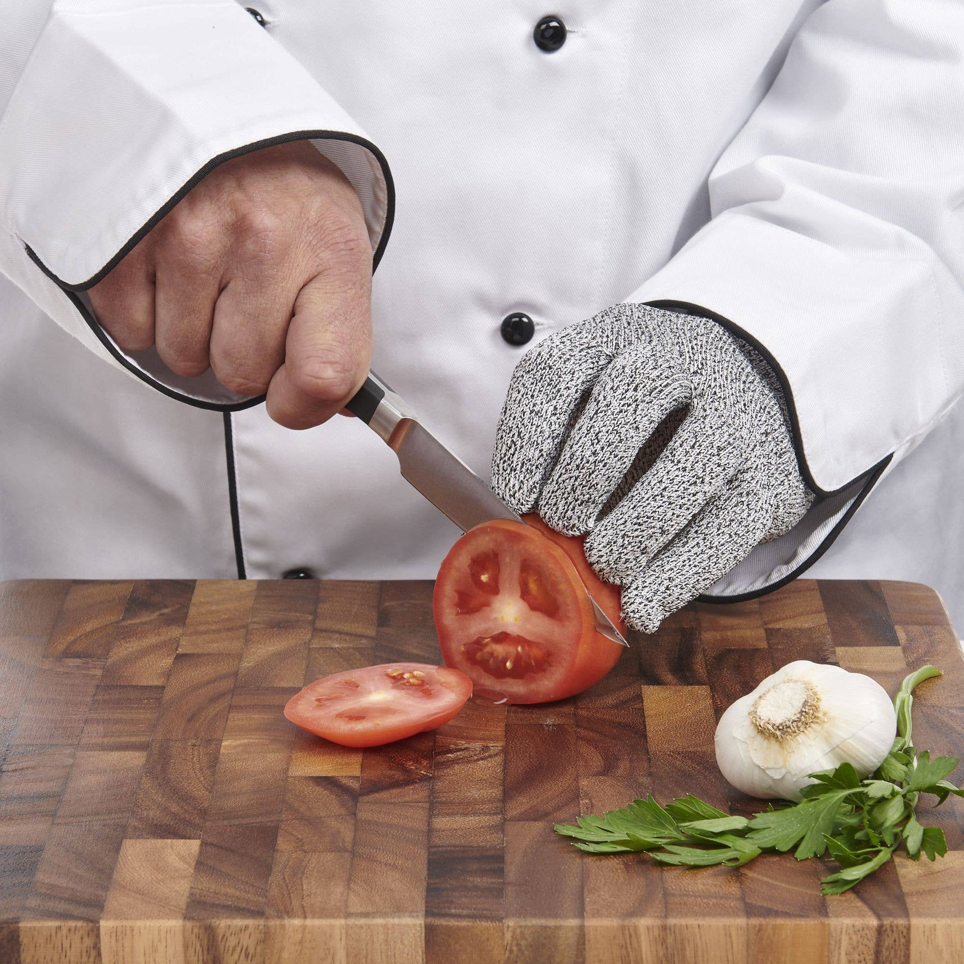 Chef cutting tomatoes on a wooden board with protective gloves