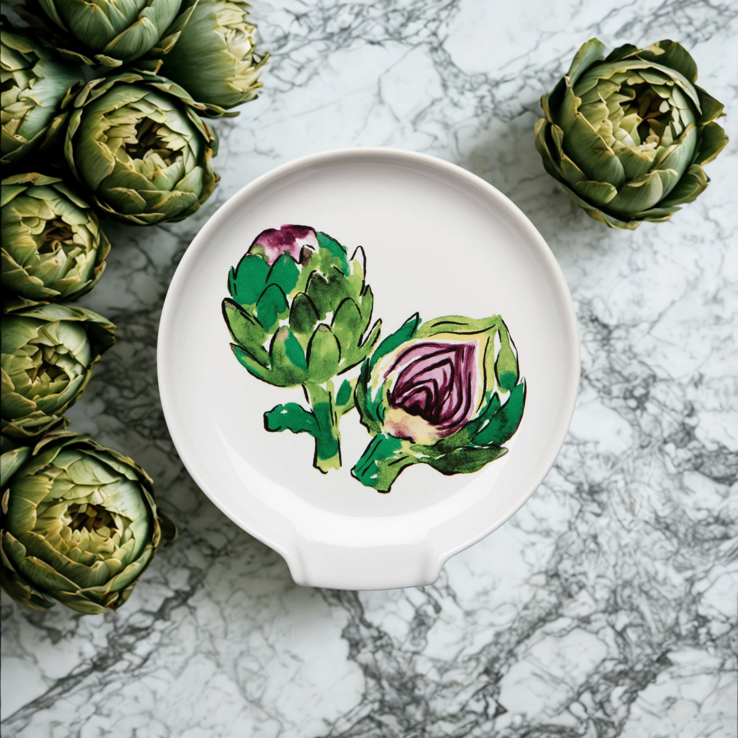 Artichokes on a marble surface with a decorative plate featuring artichoke designs.