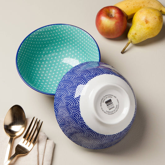 Two ceramic bowls, one blue and one green, on a table with fruit and cutlery.