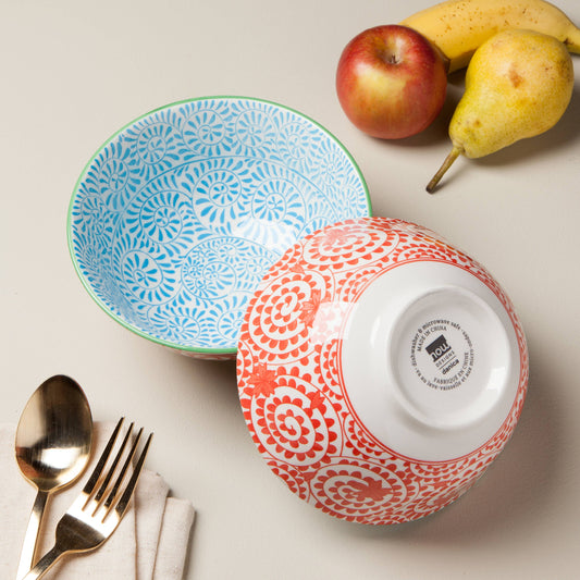 Two patterned bowls with a spoon, fork, napkin, apple, and pear on a light surface.