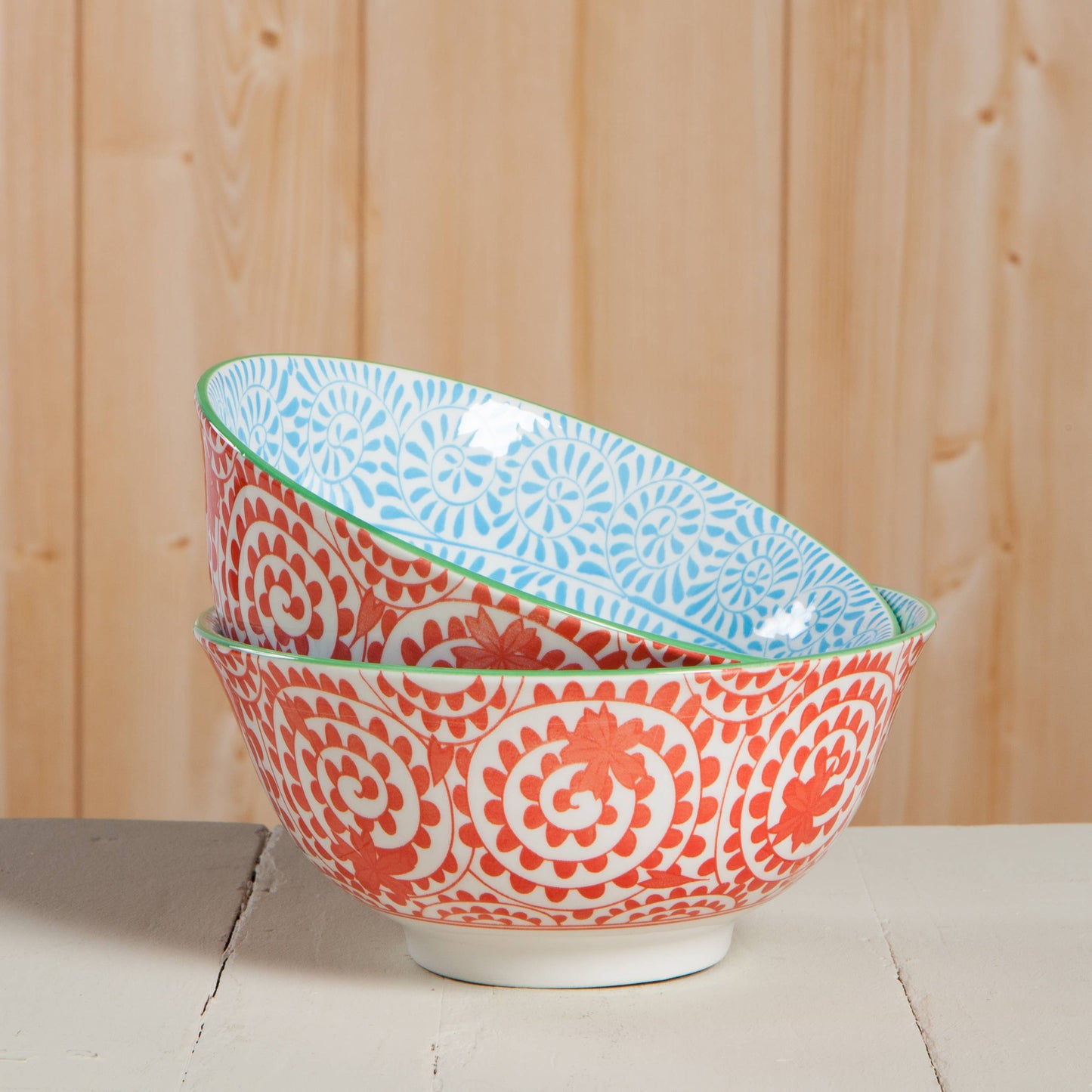 Two ceramic bowls with red and blue patterns stacked on a wooden surface.