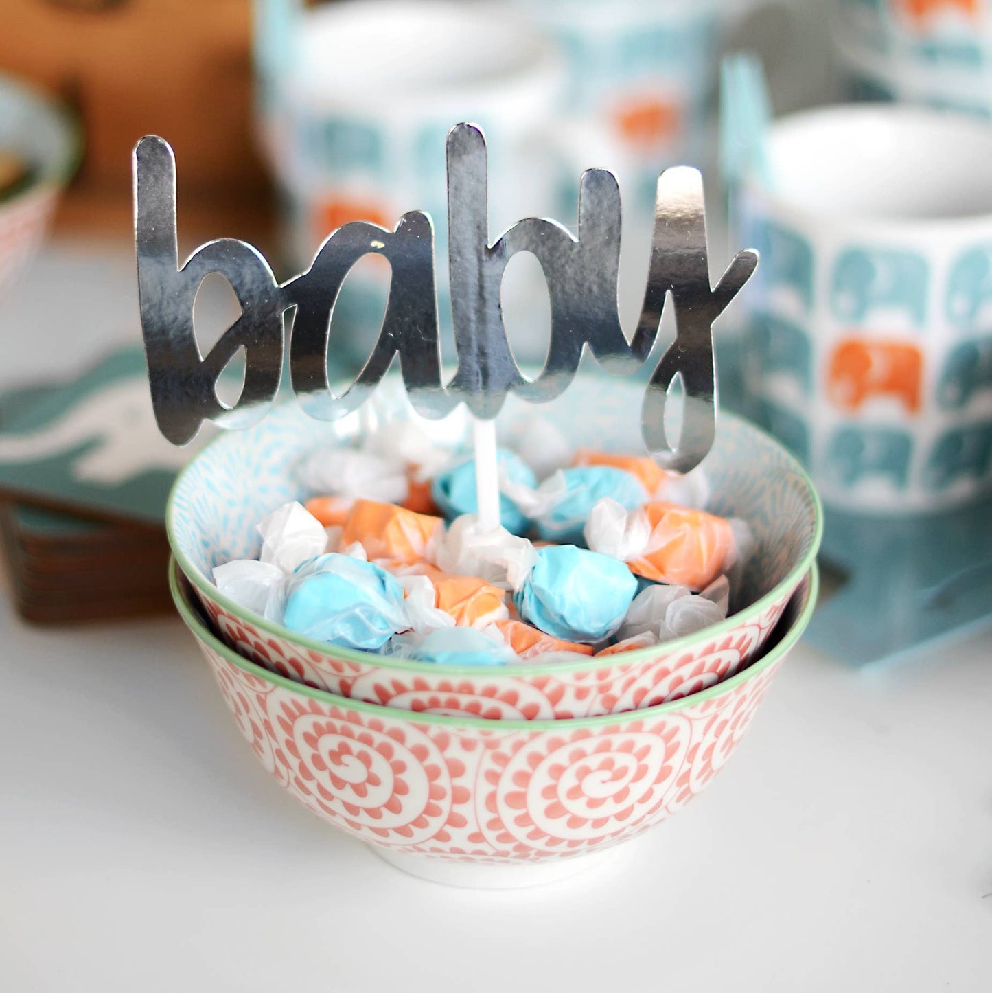 Decorative bowl with candy and 'baby' sign, surrounded by patterned bowls.