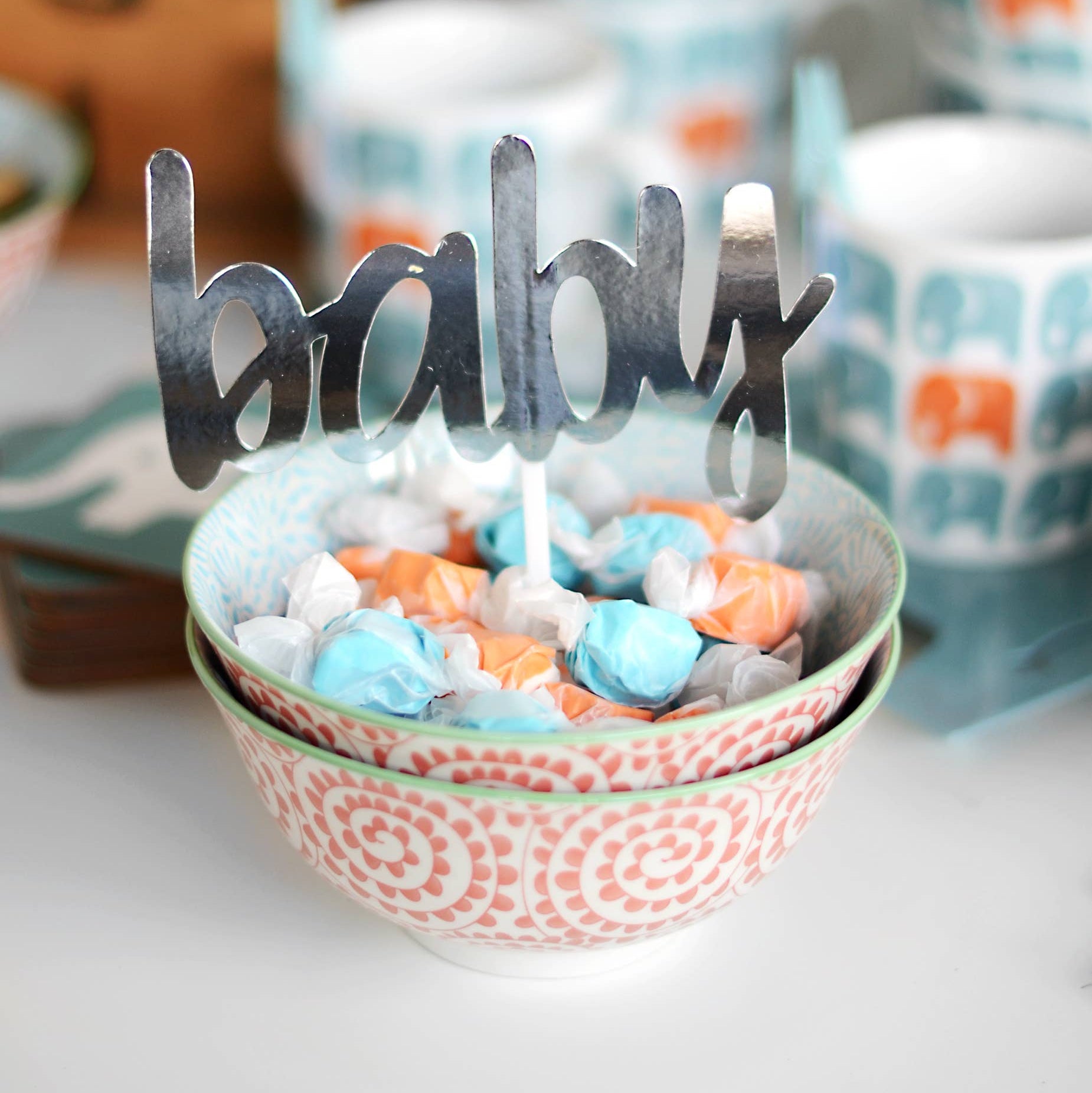 Decorative bowl with candy and 'baby' sign, surrounded by patterned bowls.