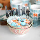 Decorative bowl with candy and 'baby' sign, surrounded by patterned bowls.