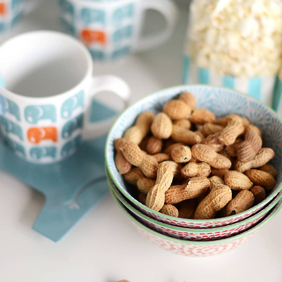 Bowl of peanuts with patterned cups and a bag of snacks on a white surface