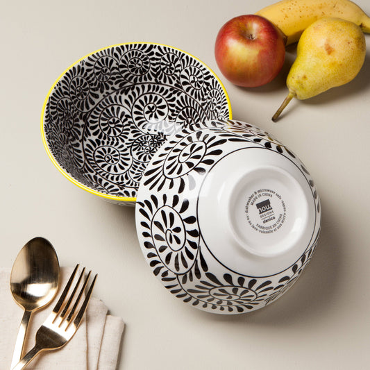 Black and white patterned bowls with a brand logo, apples, and bananas on a light surface.