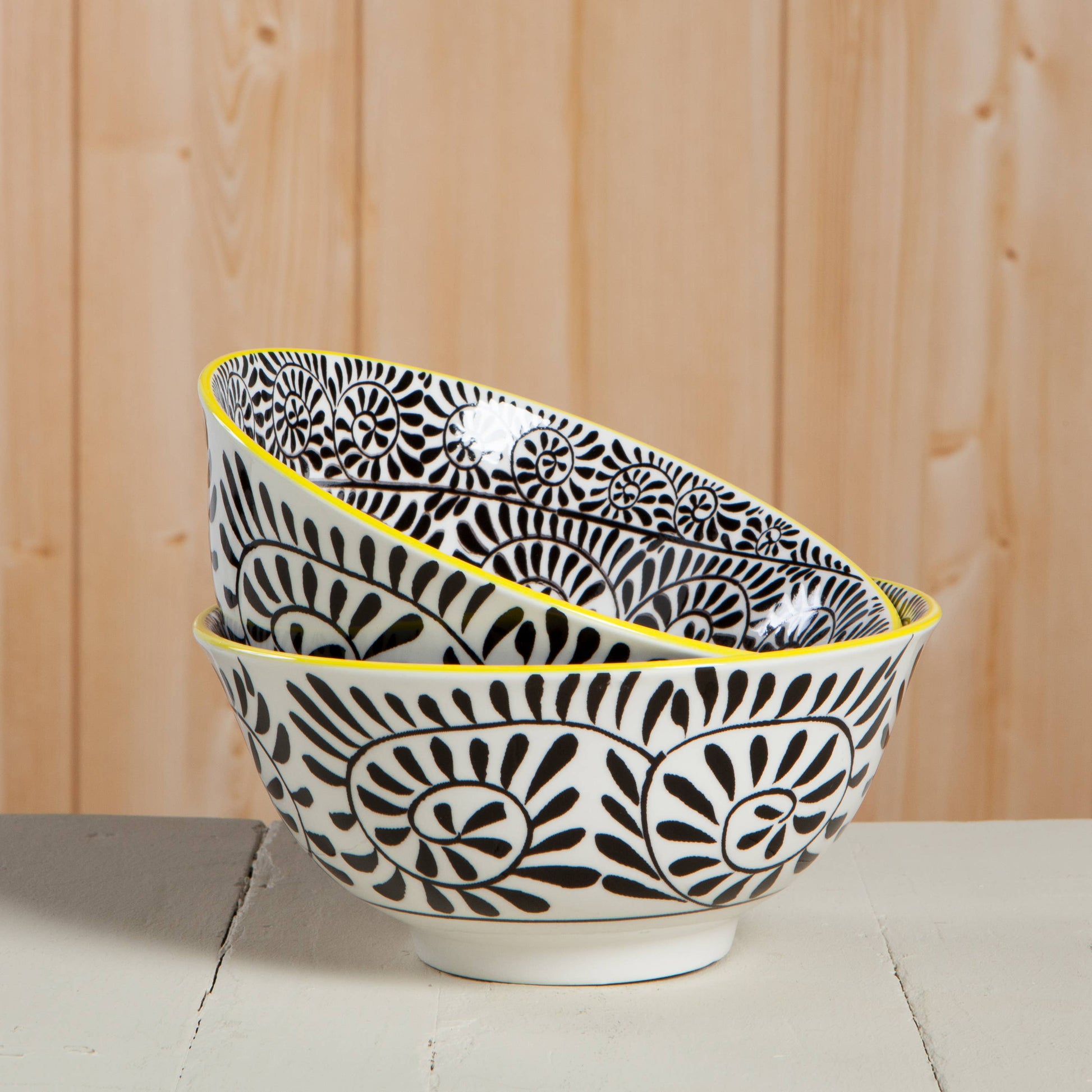 Two black and white patterned bowls with yellow rims on a wooden surface.