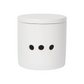 A minimalist white cylindrical container with a matching lid and three small black circular cutouts on the front, set against a solid white background.