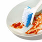 Dish brush scraping red food off of a white dish. 