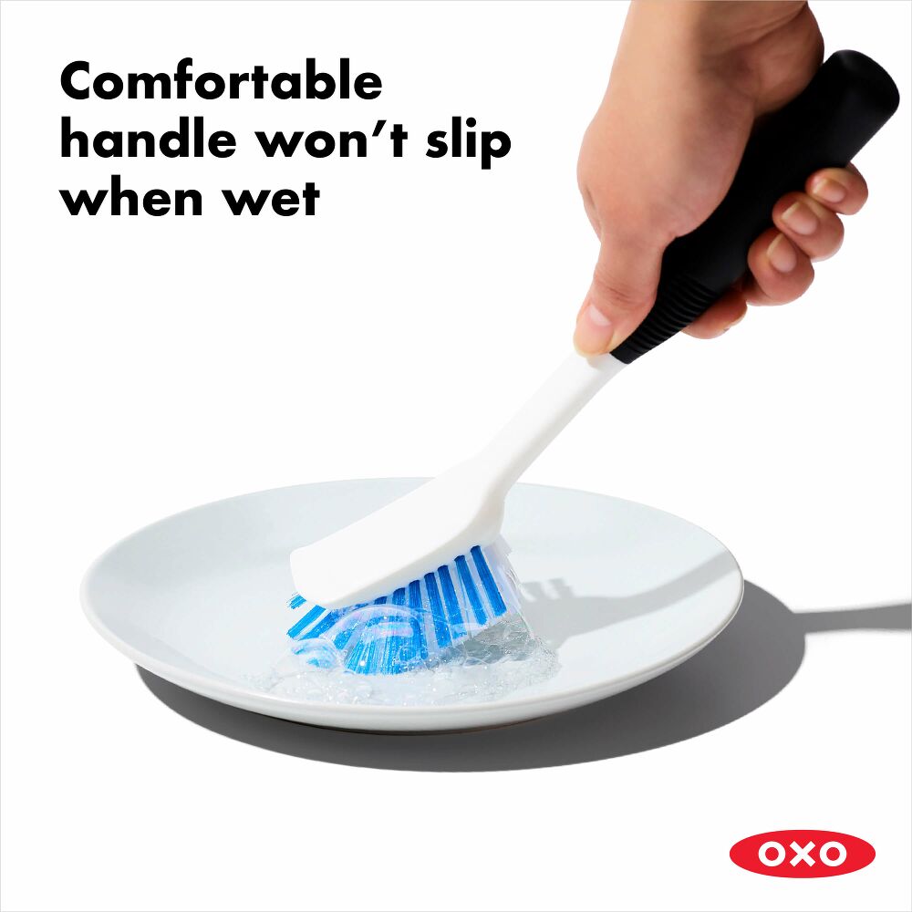 Hand using a dish brush to wash a white plate. 