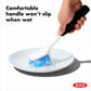 Hand using a dish brush to wash a white plate. 