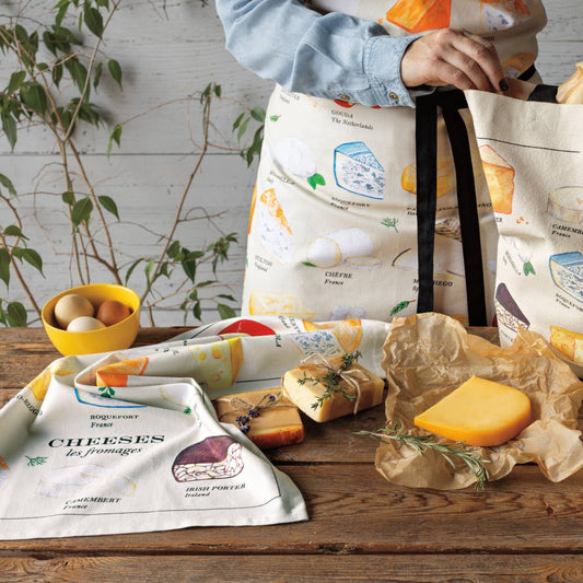 Two tote bags with cheese illustrations on a wooden table with cheese and packaging.
