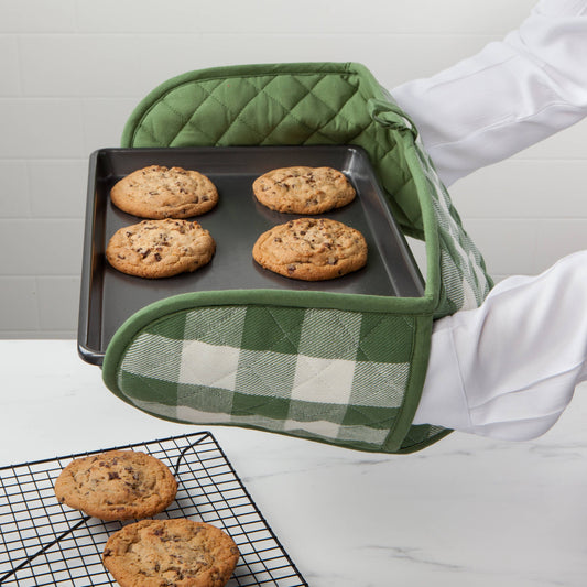Person holding a tray of cookies with green oven mitts, kitchen setting