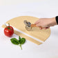 Hand using a pizza cutter on dough with a tomato and basil on a white background