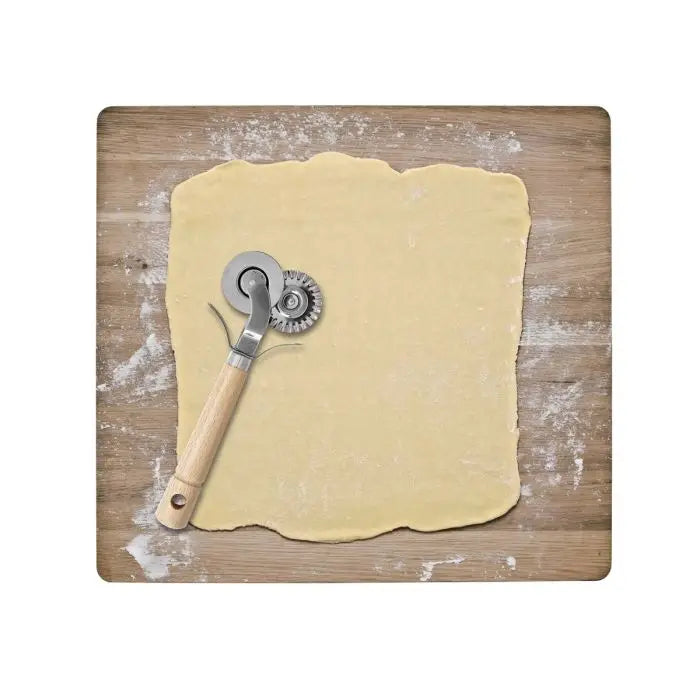 A metal and wood pastry wheel cutter resting on a rolled sheet of pale dough over a wooden board with flour dusting.