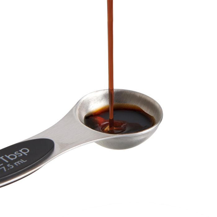Spoon with a measurement label pouring dark liquid on a white background