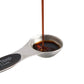 Spoon with a measurement label pouring dark liquid on a white background