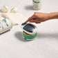 Hand interacting with a small electronic can opener on a white surface with cans in the background