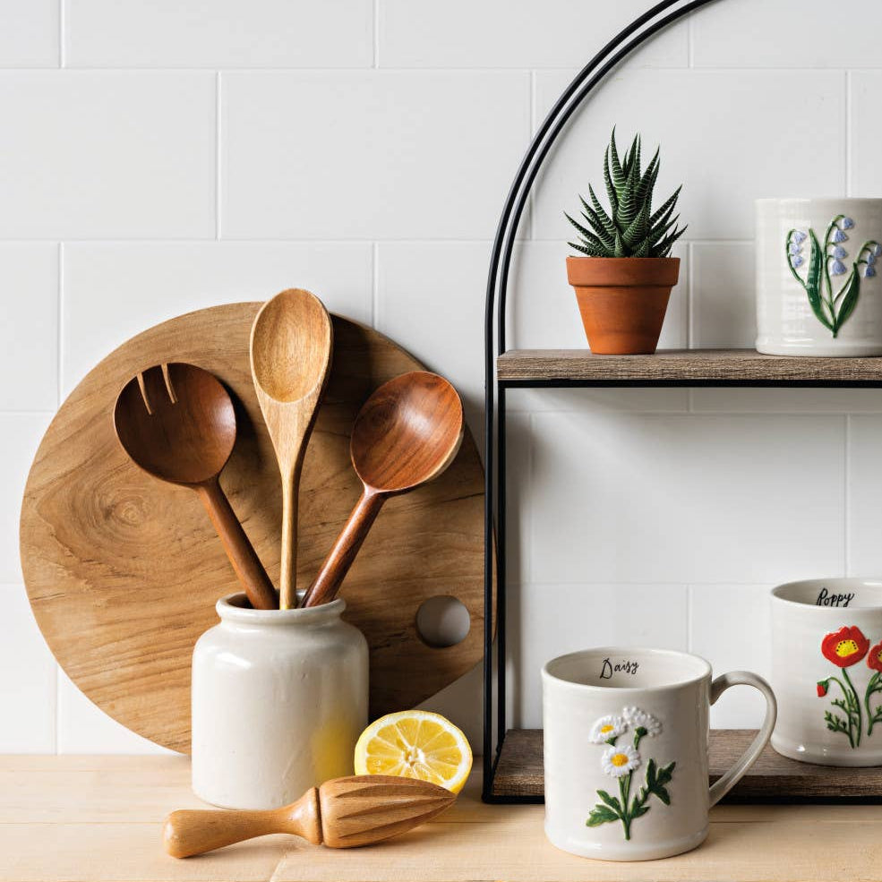 Set of mugs with floral designs on a wooden shelf with potted plants and wooden utensils.