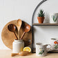 Set of mugs with floral designs on a wooden shelf with potted plants and wooden utensils.