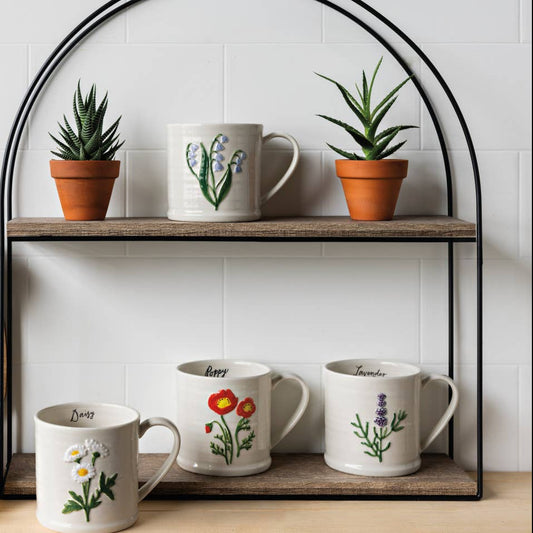 Set of mugs with floral designs on a wooden shelf with potted plants and wooden utensils.