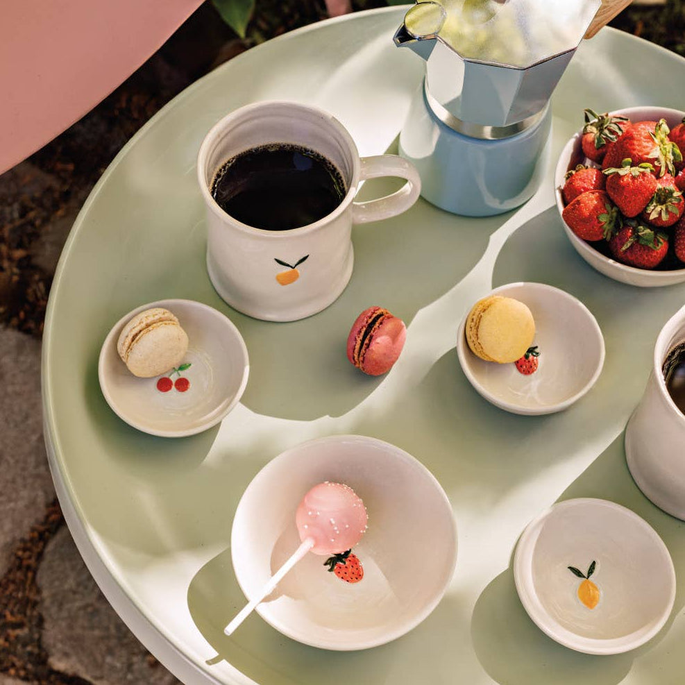 Round table with various small dishes containing pastries and a cup of coffee, set outdoors.
