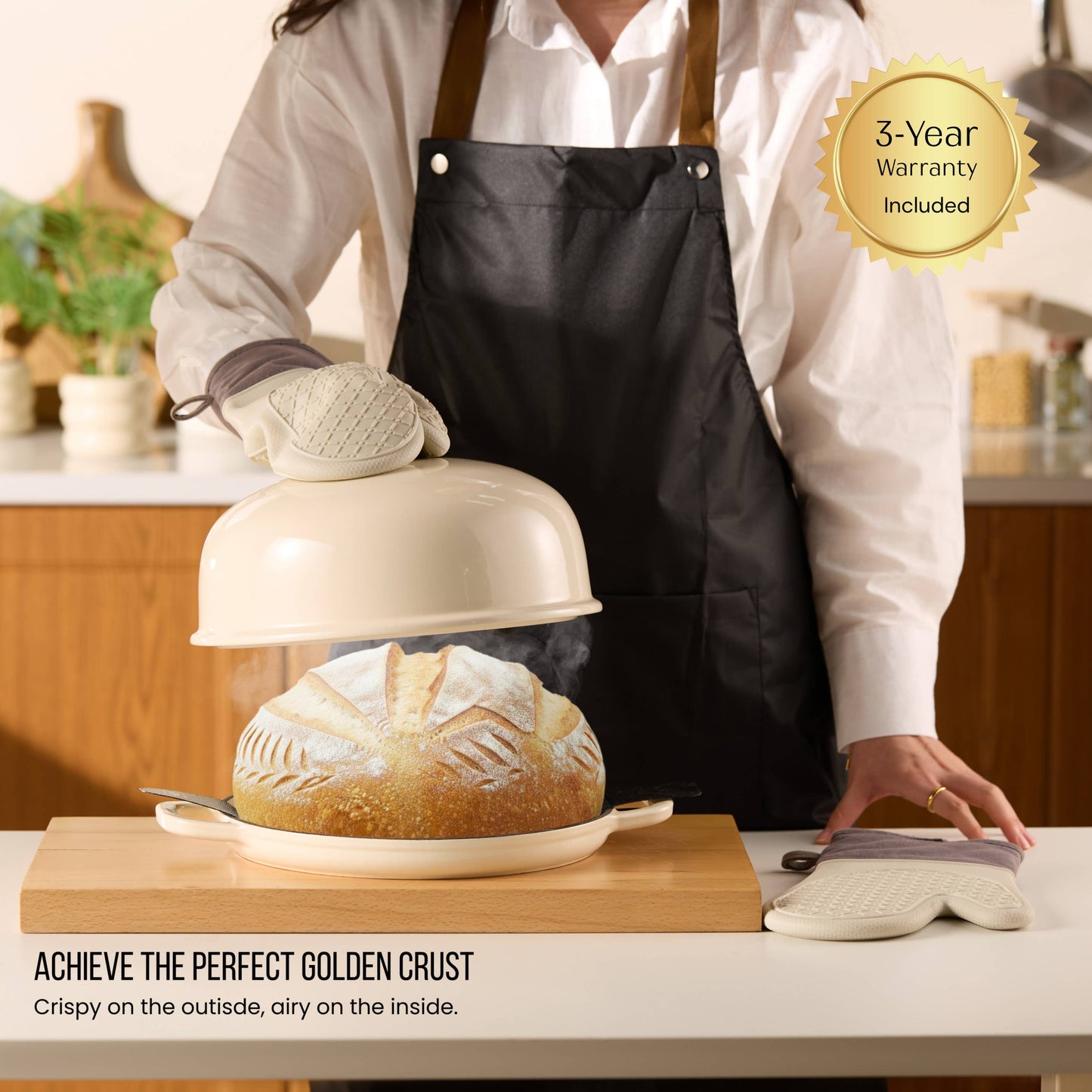 Person in a kitchen holding a bread steamer with bread inside, wearing an apron and oven mitts.