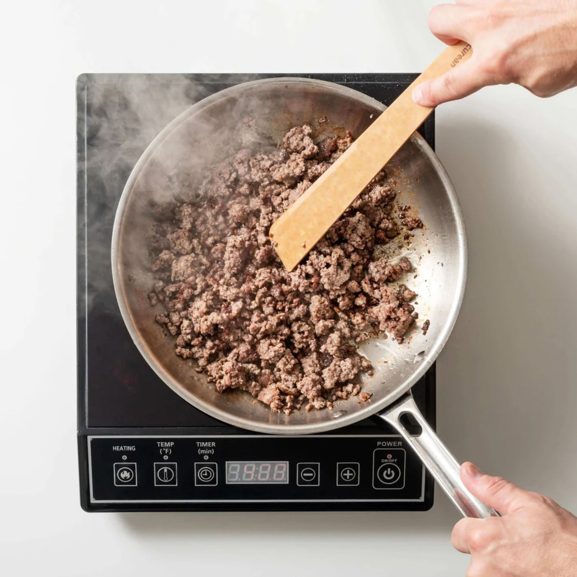 Person stirring ground meat in a frying pan on an induction cooktop.