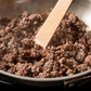 Browned ground meat in a pan with a wooden spatula