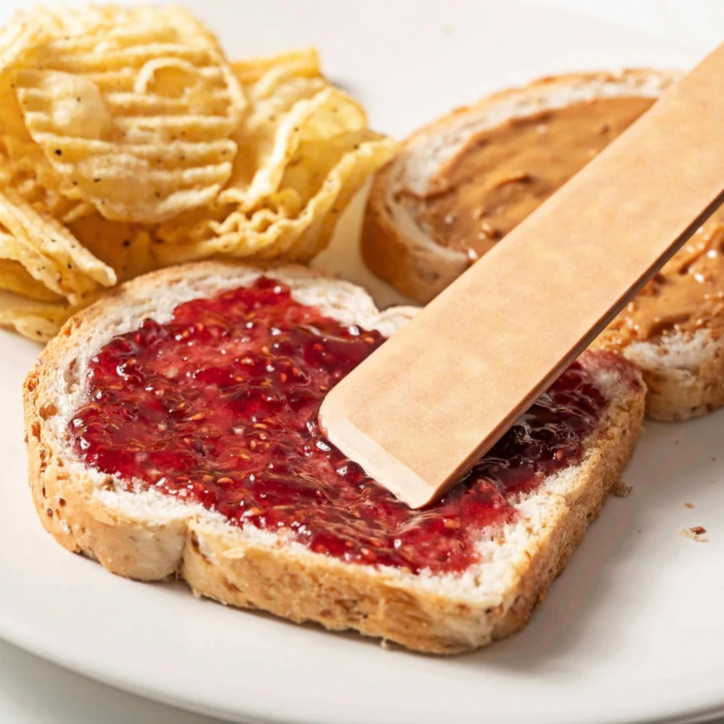 Bread with peanut butter and jelly, accompanied by potato chips on a white plate.