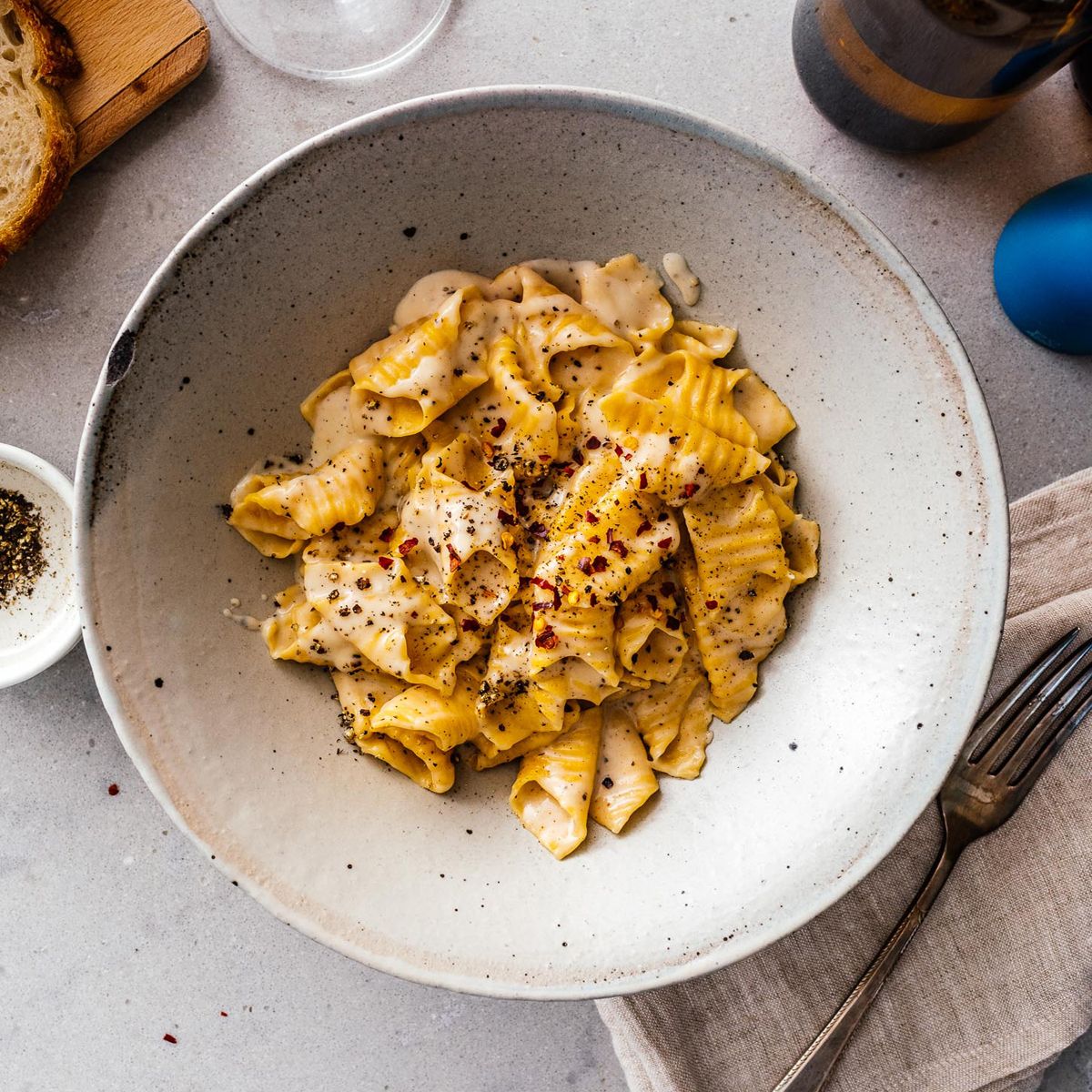 Pasta dish in a bowl on a table with a fork and napkin.