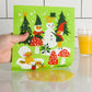 Green kitchen towel with Christmas-themed design held by a hand, with a glass of orange juice in the background.