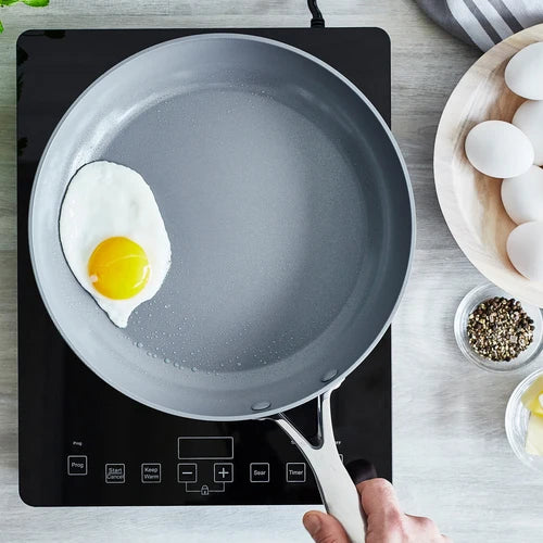 Frying pan with a single fried egg on an induction cooktop, surrounded by eggs and seasonings.