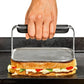 Hand using a griddle press on a cheesey sandwich on a black grill. 