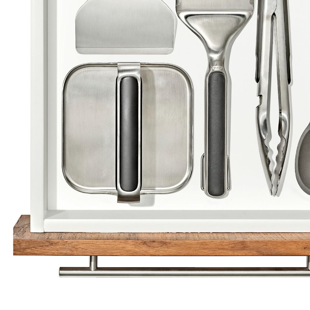 Metal griddle press in a white drawer with other kitchen tools. 