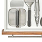 Metal griddle press in a white drawer with other kitchen tools. 