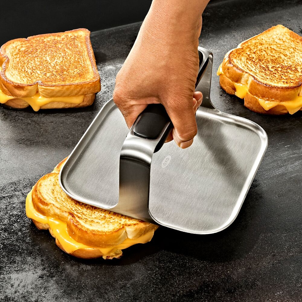 Hand using a metal grill gress on a grilled cheese sandwich. 