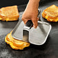 Hand using a metal grill gress on a grilled cheese sandwich. 