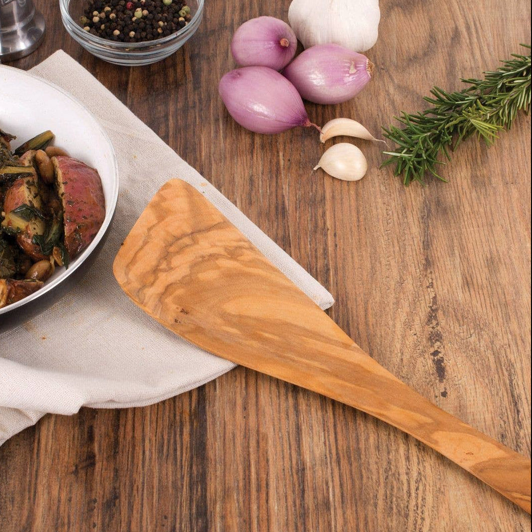 Wooden spoon on a wooden table with a bowl of food, onions, and rosemary.