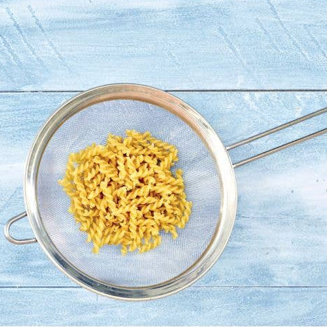 Yellow pasta in a metal strainer on a light blue wooden surface