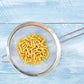 Yellow pasta in a metal strainer on a light blue wooden surface
