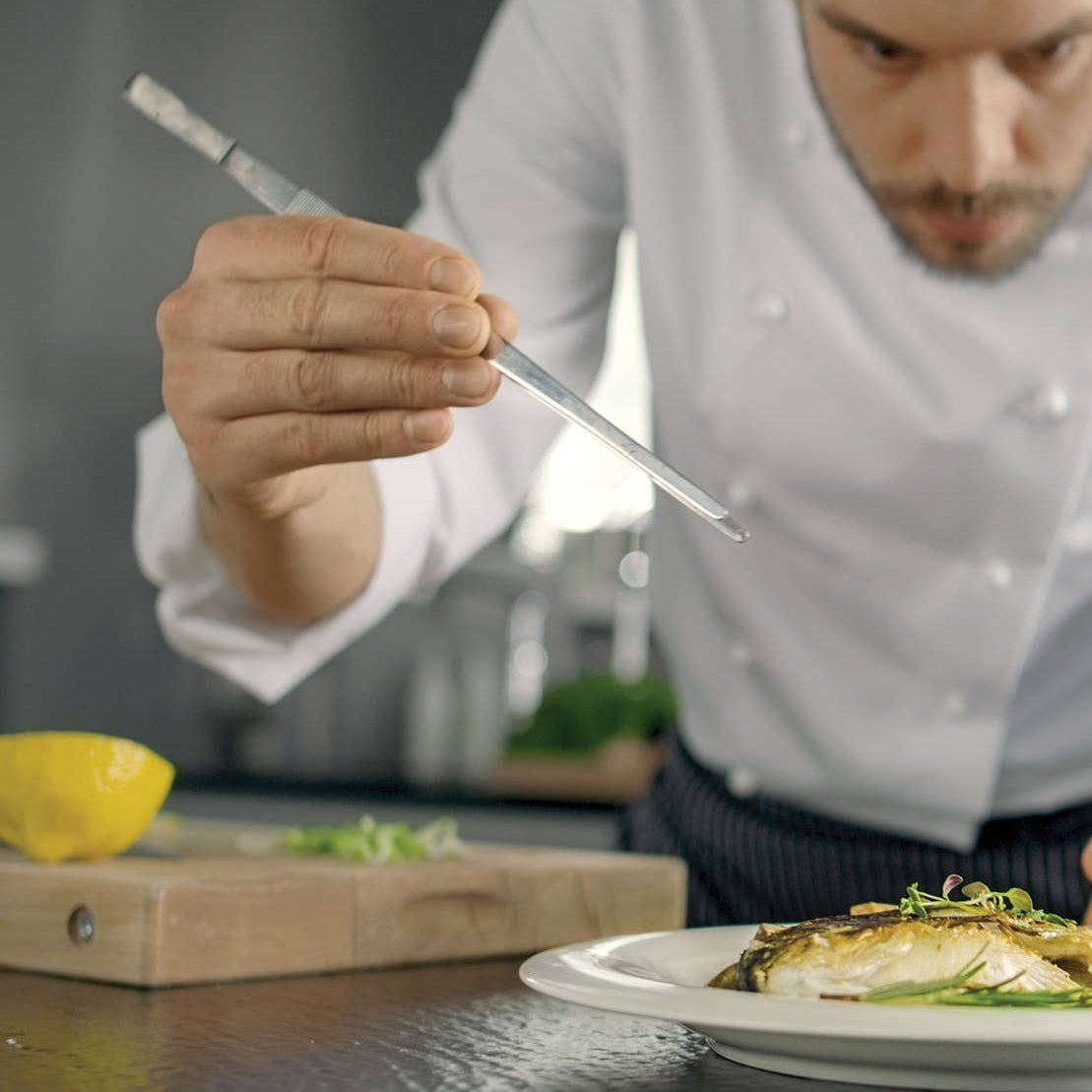 Chef garnishing a dish with a lemon wedge in a professional kitchen setting