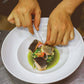 Person garnishing a dish with fish and vegetables on a white plate.
